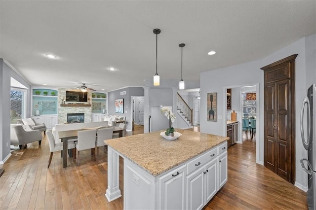 kitchen featuring light wood-style flooring, a ceiling fan, open floor plan, white cabinetry, and a fireplace