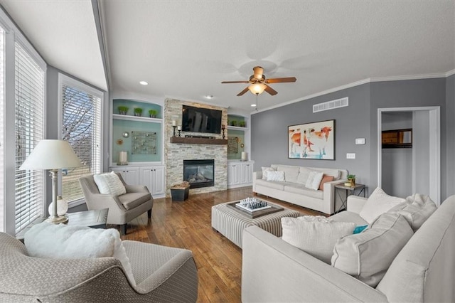 living area with a stone fireplace, wood finished floors, visible vents, and a textured ceiling