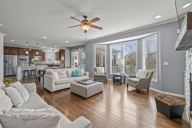 living area featuring dark wood-style floors, a stone fireplace, plenty of natural light, and a ceiling fan