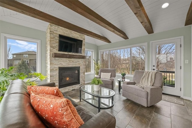 living room featuring beam ceiling, a fireplace, baseboards, and stone tile flooring