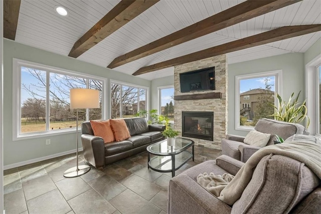 living room with baseboards, a stone fireplace, vaulted ceiling with beams, and a healthy amount of sunlight