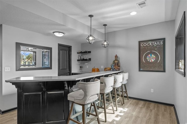 bar featuring light wood-type flooring, visible vents, pendant lighting, wet bar, and baseboards