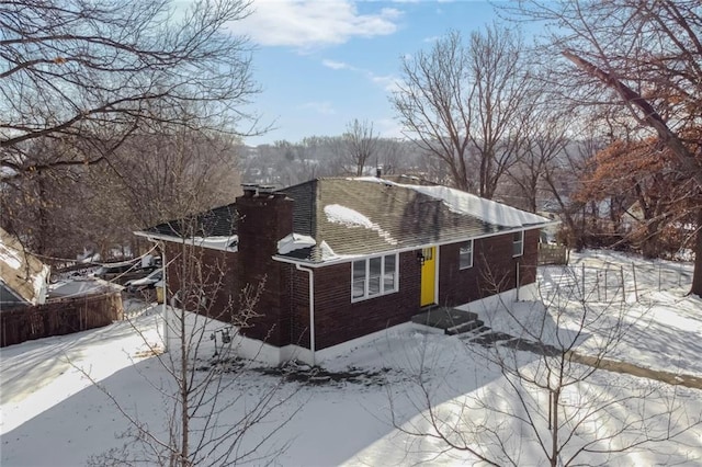 view of snow covered exterior featuring brick siding, a shingled roof, and fence