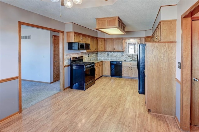 kitchen featuring tasteful backsplash, light wood-type flooring, light countertops, black appliances, and a sink