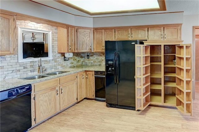 kitchen featuring tasteful backsplash, light stone counters, light wood-style flooring, black appliances, and a sink