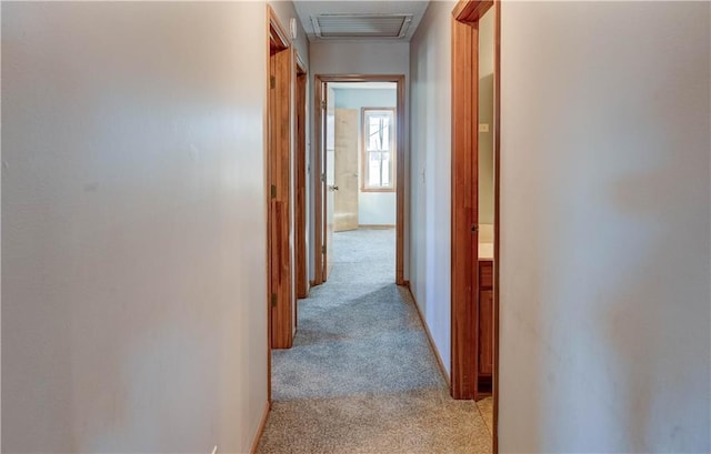 hallway with light carpet, visible vents, and baseboards