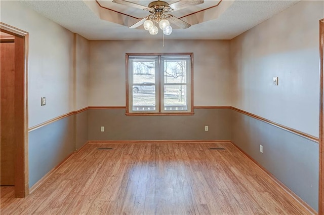 empty room featuring a textured ceiling, a ceiling fan, a tray ceiling, and wood finished floors