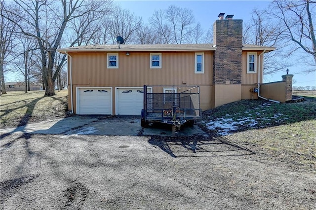 rear view of property featuring aphalt driveway, a chimney, and a garage