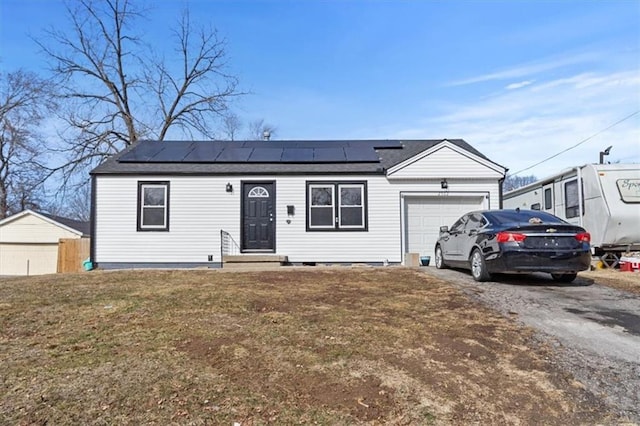 ranch-style home featuring entry steps, a garage, solar panels, driveway, and a front lawn