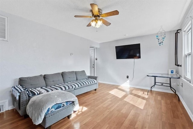 living area with ceiling fan, a textured ceiling, baseboards, and wood finished floors