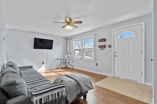 living room featuring ceiling fan, a textured ceiling, baseboards, and wood finished floors