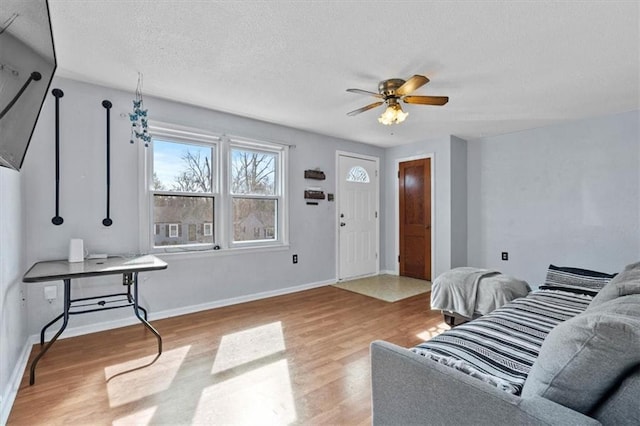 living room with a textured ceiling, ceiling fan, light wood-style flooring, and baseboards