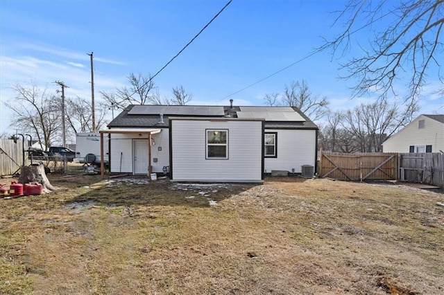 rear view of house with solar panels, central AC unit, a lawn, and a fenced backyard