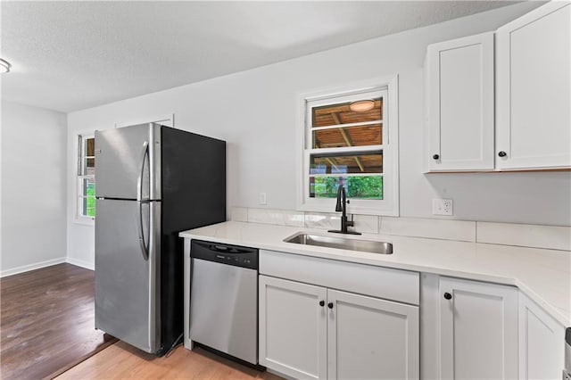 kitchen featuring stainless steel appliances, a sink, light wood finished floors, white cabinets, and a textured ceiling