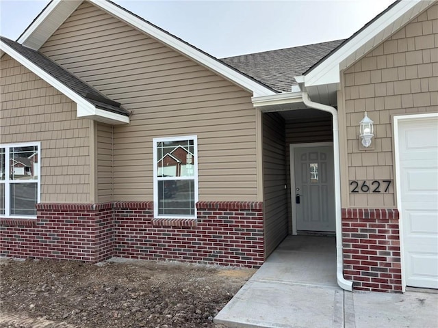 view of exterior entry featuring brick siding and roof with shingles