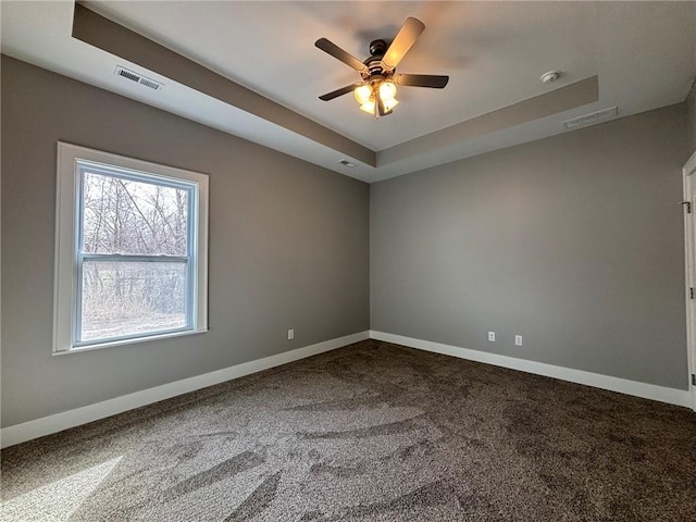 empty room featuring a raised ceiling, baseboards, visible vents, and dark colored carpet