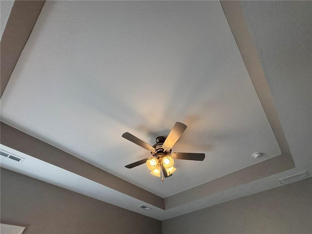 interior details with a raised ceiling, a ceiling fan, and visible vents