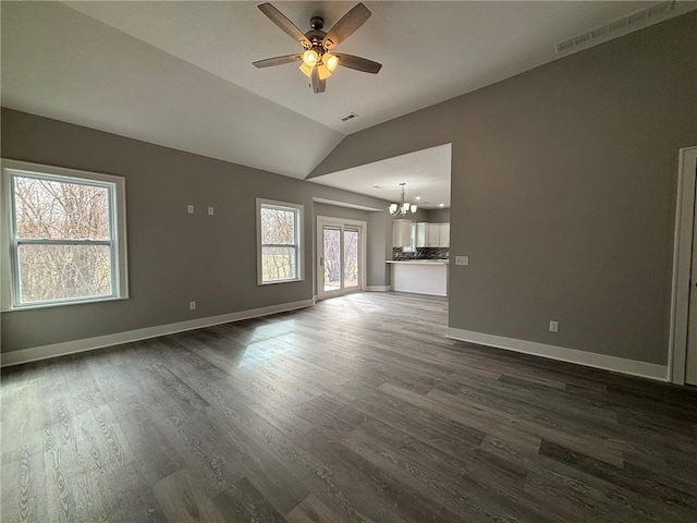 unfurnished living room featuring dark wood finished floors, vaulted ceiling, ceiling fan with notable chandelier, and baseboards