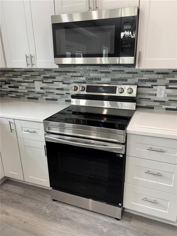 kitchen with stainless steel appliances, light wood-style floors, decorative backsplash, and light countertops