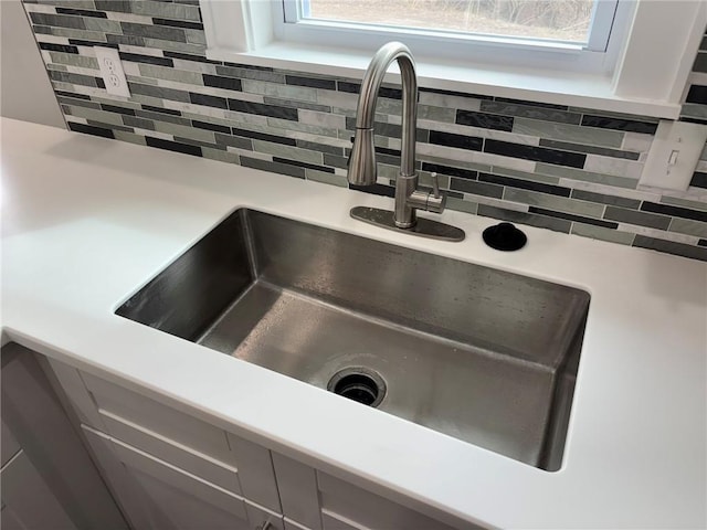 details featuring light countertops, white cabinets, backsplash, and a sink