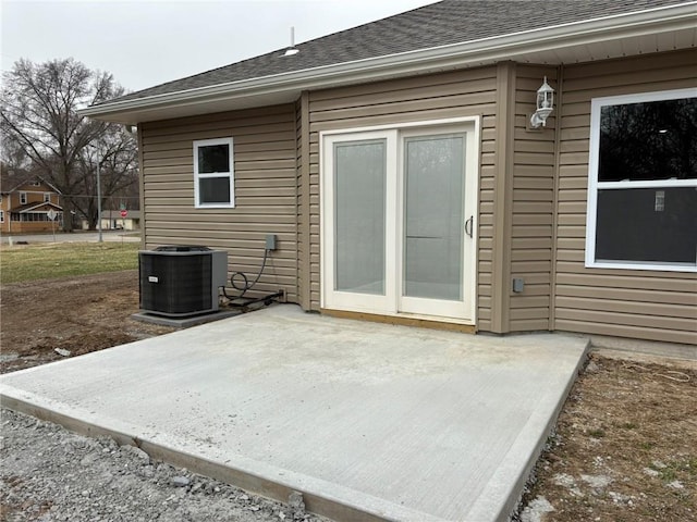 exterior space with a patio area, central AC unit, and roof with shingles