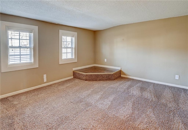 carpeted spare room featuring a textured ceiling and baseboards