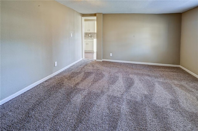 unfurnished room featuring a textured ceiling, carpet, and baseboards