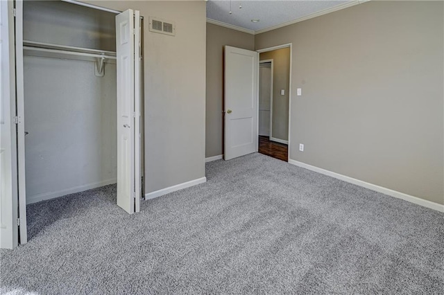 unfurnished bedroom with carpet flooring, visible vents, baseboards, ornamental molding, and a closet