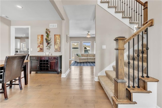 entrance foyer with ceiling fan, baseboards, light wood-type flooring, visible vents, and stairway
