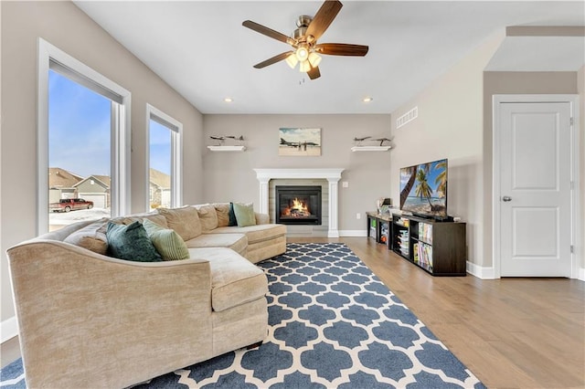 living area featuring ceiling fan, visible vents, wood finished floors, baseboards, and a glass covered fireplace