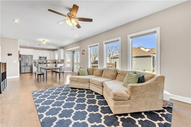 living room with a ceiling fan, baseboards, recessed lighting, and light wood-style floors