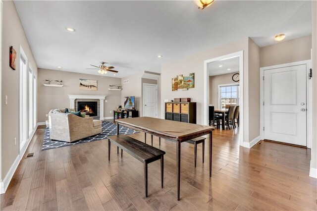 dining space with baseboards, a ceiling fan, a warm lit fireplace, and wood finished floors