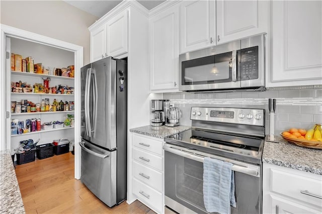 kitchen with tasteful backsplash, light stone countertops, white cabinetry, stainless steel appliances, and light wood-style flooring