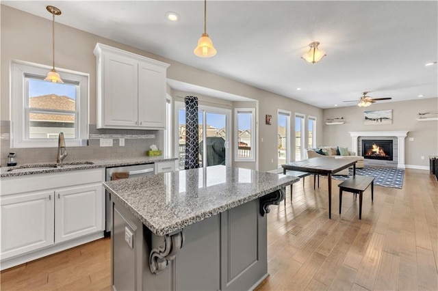 kitchen featuring a ceiling fan, a glass covered fireplace, white cabinets, tasteful backsplash, and a sink