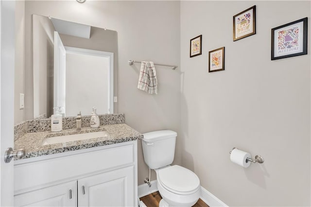 half bathroom with vanity, baseboards, and toilet