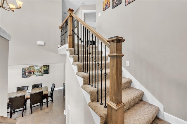 stairway with wood finished floors, baseboards, a chandelier, and a towering ceiling