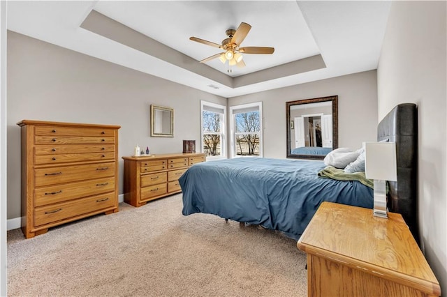 bedroom with light colored carpet, a raised ceiling, ceiling fan, and baseboards