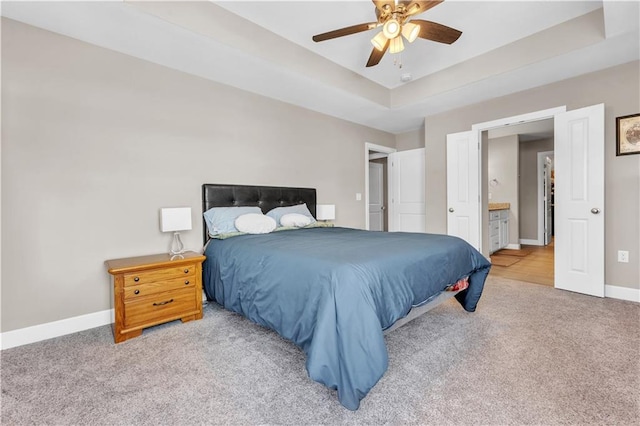 bedroom featuring ceiling fan, carpet floors, baseboards, a raised ceiling, and ensuite bathroom