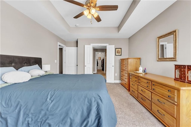 bedroom featuring baseboards, ceiling fan, a tray ceiling, and light carpet