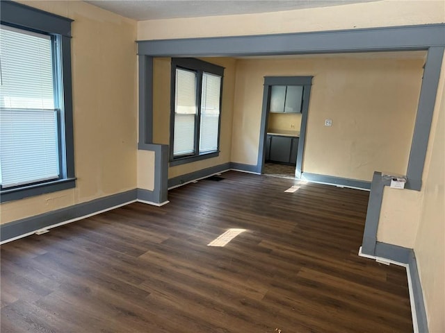 empty room with dark wood-style floors, plenty of natural light, and baseboards