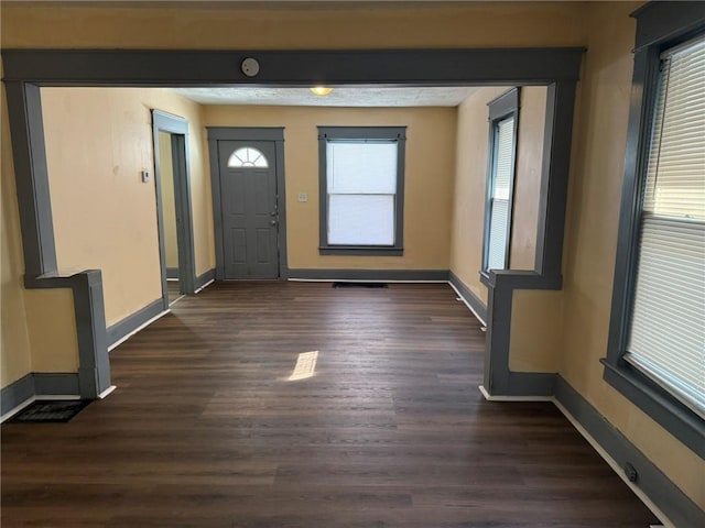 foyer entrance with dark wood-style floors, visible vents, and baseboards