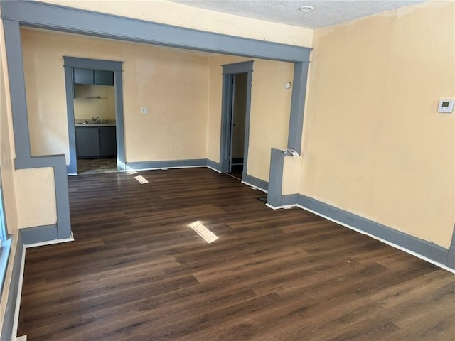 unfurnished room featuring a sink, a textured ceiling, dark wood finished floors, and baseboards