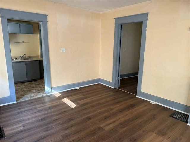 unfurnished room with dark wood-style floors, baseboards, visible vents, and a sink