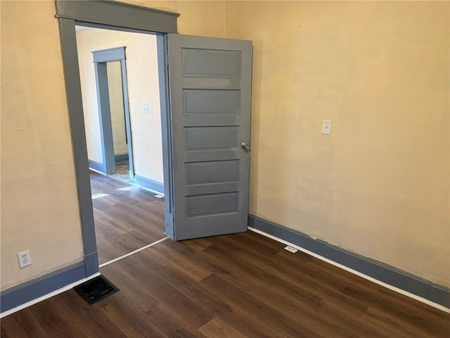 empty room featuring dark wood-style floors, baseboards, and visible vents