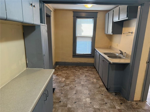 kitchen with baseboards, light countertops, a sink, and gray cabinetry