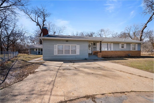 ranch-style house with concrete driveway, brick siding, fence, and a chimney