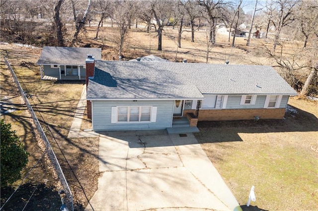 view of front facade with brick siding, a chimney, concrete driveway, and roof with shingles