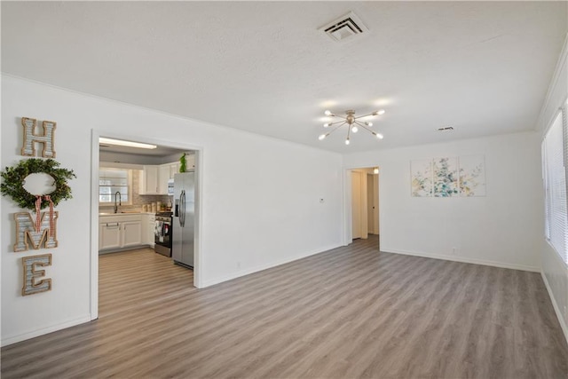 empty room with light wood finished floors, baseboards, visible vents, and a sink