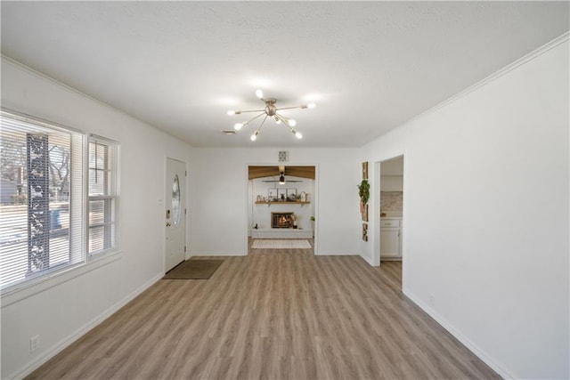 unfurnished living room with baseboards, a lit fireplace, light wood finished floors, and an inviting chandelier