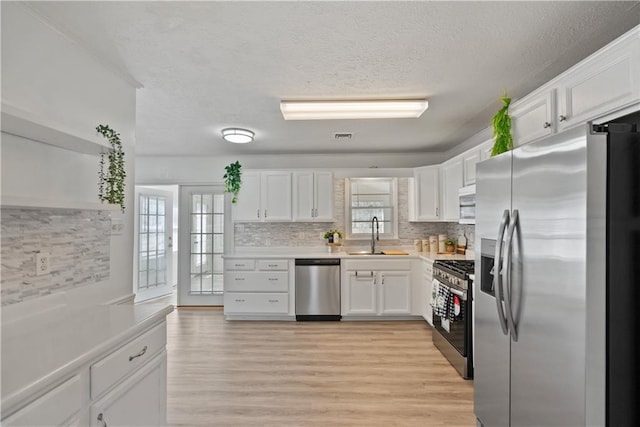 kitchen with stainless steel appliances, a sink, white cabinets, light countertops, and tasteful backsplash